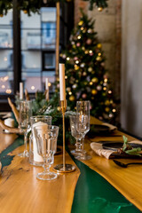 Christmas table setting in rustic style with candles, plates, glasses and eco decors on wooden festive table.New year decorations with fir branches, golden balls, pine cones. Cozy winter holidays.