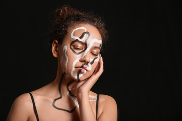 Beautiful young African-American woman with paint on her body against dark background