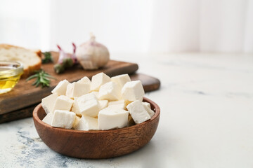 Wooden bowl with pieces of feta cheese on light table