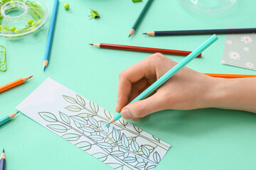 Woman coloring bookmark on color background