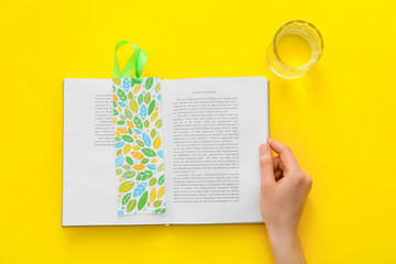 Woman with glass of water reading book on color background