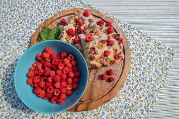 Bowl with fresh raspberries, and pie with raspberries and rhubarb on the wooden board