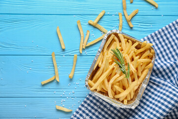 Box with tasty french fries on color wooden background