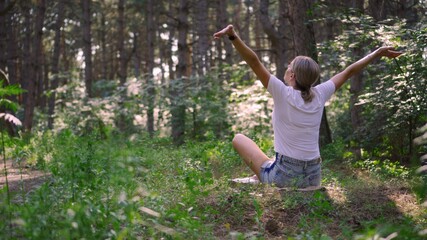 A young woman enjoys harmony with nature in a green forest. She enjoys breathing in the air and...