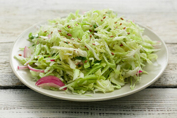 Plate with tasty cabbage salad on light wooden table