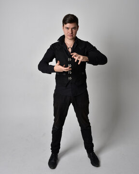 Full length portrait of a brunette man wearing black shirt and gothic waistcoat.  Standing pose isolated  against a grey studio background.
