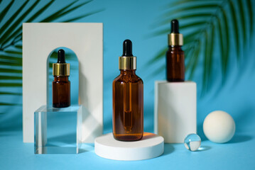 Naklejka premium Three amber glass bottles with trendy geometric shapes on a blue background.. White pedestal and arch. Green tropical palm leaves. Skincare products , natural cosmetic. Beauty concept for face care