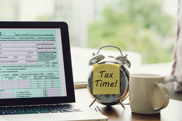 Tax time concept. tax time on a post-it on alarm clock and Individual income tax return form...