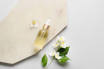Board with bottle of essential oil and jasmine flowers on grey background
