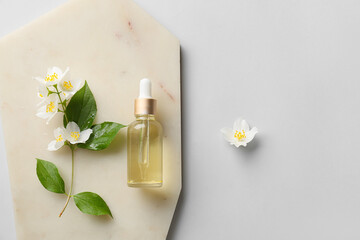 Board with bottle of essential oil and jasmine flowers on grey background