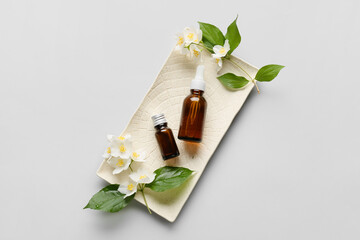 Obraz na płótnie Canvas Plate with bottles of essential oil and jasmine flowers on grey background