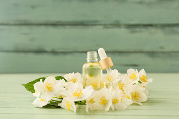 Bottle of essential oil and jasmine flowers on color wooden background