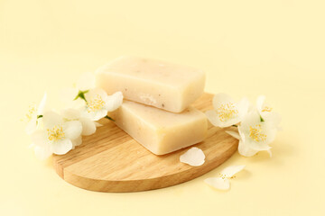 Board with soap bars and jasmine flowers on color background