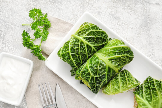 Plate with stuffed cabbage leaves and sour cream on light background