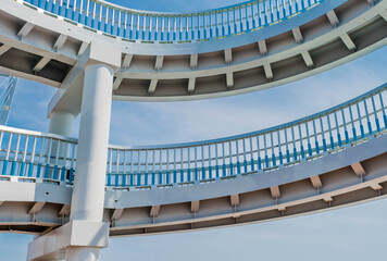 Two parts of a circular ramp of pedestrian bridge with blue cloudy sky in background.