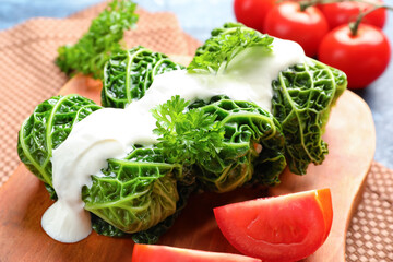 Board with stuffed cabbage leaves, sour cream and tomatoes on color background, closeup