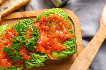 Board with stuffed cabbage leaves, tomato sauce and parsley on table, closeup