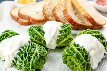 Plate with stuffed cabbage leaves, sour cream and bread, closeup
