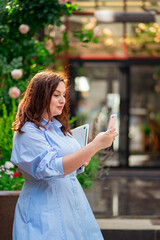 woman stands on street at entrance to building with a laptop and smartphone.