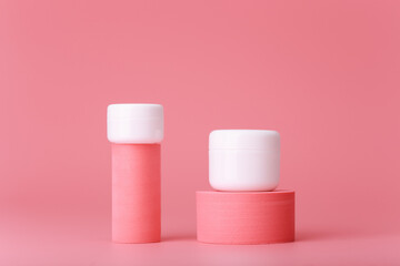 Modern trendy set of two white cosmetic jars on pink geometric shapes for product presentation against pink background. Concept of skin care and beauty