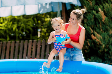 Fototapeta na wymiar Mom and daughter have fun in the pool in the garden, dipping into the warm water