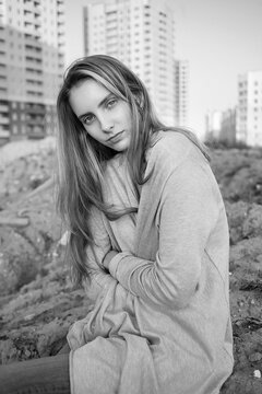 beautiful young woman in grey blouse, jeans. black and white portrait of cute attractive model, buildings on background. caucasian skinny natural pretty female sitting on ground outdoors