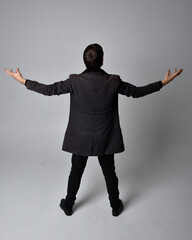 Full length portrait of a brunette man wearing black leather coat.  Standing pose facing backwards,...