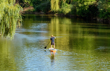 Rear view of man standing and paddling on sup board on green river in summer.