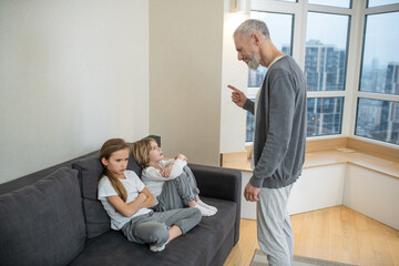 Gray-haired bearded man talking to his kids and looking unsatisfied