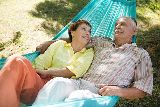 Happy senior couple rest in a hammock in a summer park or garden. Concept of friendly family.