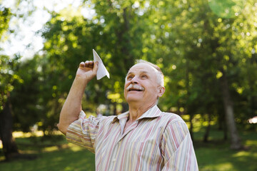 Senior man fly paper airplanes in the park. Summer holiday
