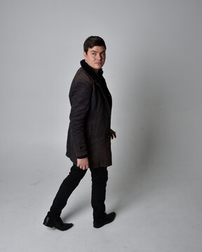 Full length portrait of a brunette man wearing black leather coat.  Standing pose facing backwards, walking away from the camera isolated  against a grey studio background.