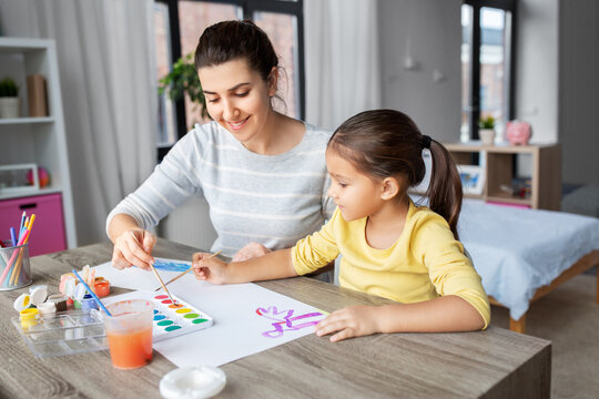 family, motherhood and leisure concept - mother spending time with her little daughter drawing with colors at home