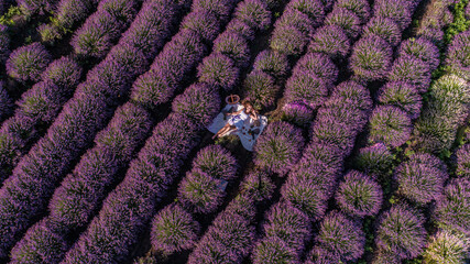 Beautiful girl in white dress on white bedspread in lavender field, shot from drone during sunrise
