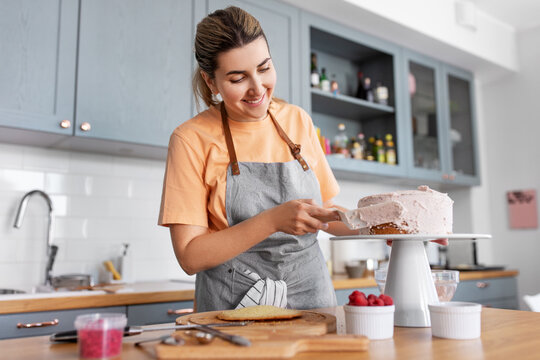 culinary, baking and cooking food concept - happy smiling young woman making layer cake and spreading topping cream on kitchen at home - Powered by Adobe