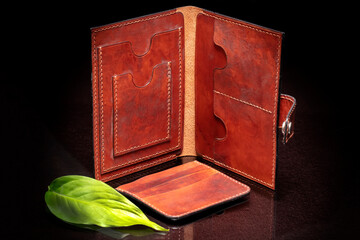 Leather brown open purse and green leaf on a dark background.