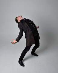 Full length portrait of a brunette man wearing black leather coat.  Standing pose isolated against a grey studio background.