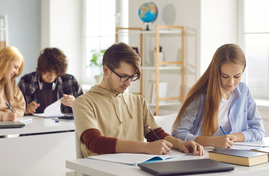 Concentrated Focused Diverse Teenager Students Group Writing Exam Taking Test Essay University Assignment Sitting At Desk With Books And Stationery In High School Classroom. Education, Learning