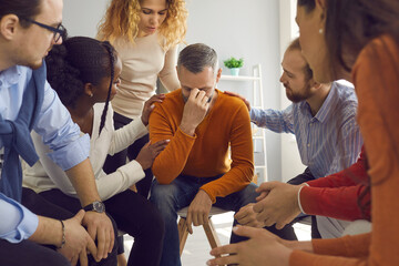 Diverse empathetic people in group therapy session comforting mature man going through difficult life period. Team of patients sharing problems and helping each other deal with grief or addiction