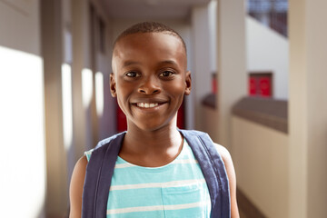 Portrait of smiling african american schoolboy wearing schoolbag standing in school corridor