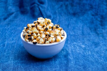 Roasted Maize or Corn Seeds in a Bowl Isolated on Blue Fabric Background with Copy Space