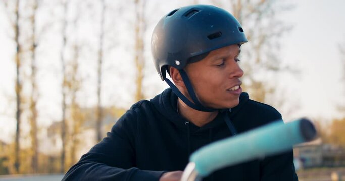 Close-up of face of handsome boy with dark complexion, sitting on bike leaning against handlebars, helmet on head, sitting in park on ramp, looking around, waiting for someone, friends