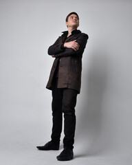 Full length portrait of a brunette man wearing black leather coat.  Standing pose isolated against a grey studio background.