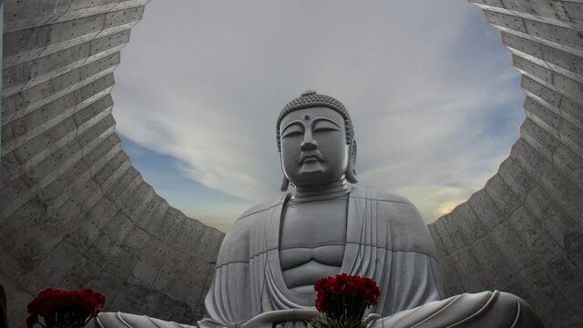 Superimposed or double exposures of sitting giant & peaceful Buddha statue inside Hill of the Buddha with a beautiful orange sun set. A Buddhist shrine at Makomanai Takino Cemetery, Sapporo, Hokkaido.