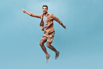 Obraz premium Cool happy man in brown trendy shirt and striped orange and yellow shorts looking into camera, smiling and funny jumping..