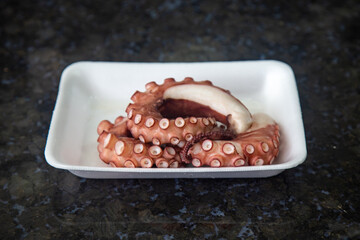 Octopus tentacles on white tray with dark background in selective focus
