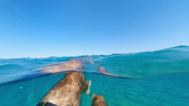 Split-shot, stunning view of a tourist swimming on a beautiful and turquoise water. Caprera, La Maddalena Archipelago, Sardinia, Italy. Over-under shot, half underwater, half sky.