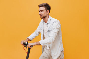 Fototapeta na wymiar Bearded fashionable man with brown hair in t-shirt and white shirt looking away and posing with scooter on isolated background..
