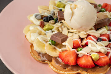 Heart waffle with banana and strawberry with gummy candy and ice cream on it.