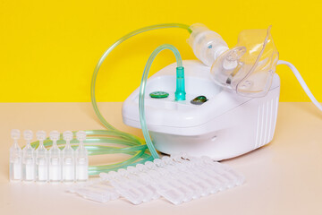 Fototapeta na wymiar Coronavirus treatment concept. An inhaler device with nebulizer mask or medical face mask for treatment of the respiratory tract and a lot of ampoules over yellow background.